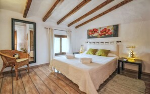 A bedroom with a large bed, a wicker chair, a painting, and a nightstand with a lamp. - Country House 'Cadernera' with Private Pool, Wi-Fi and Air Conditioning (Búger)