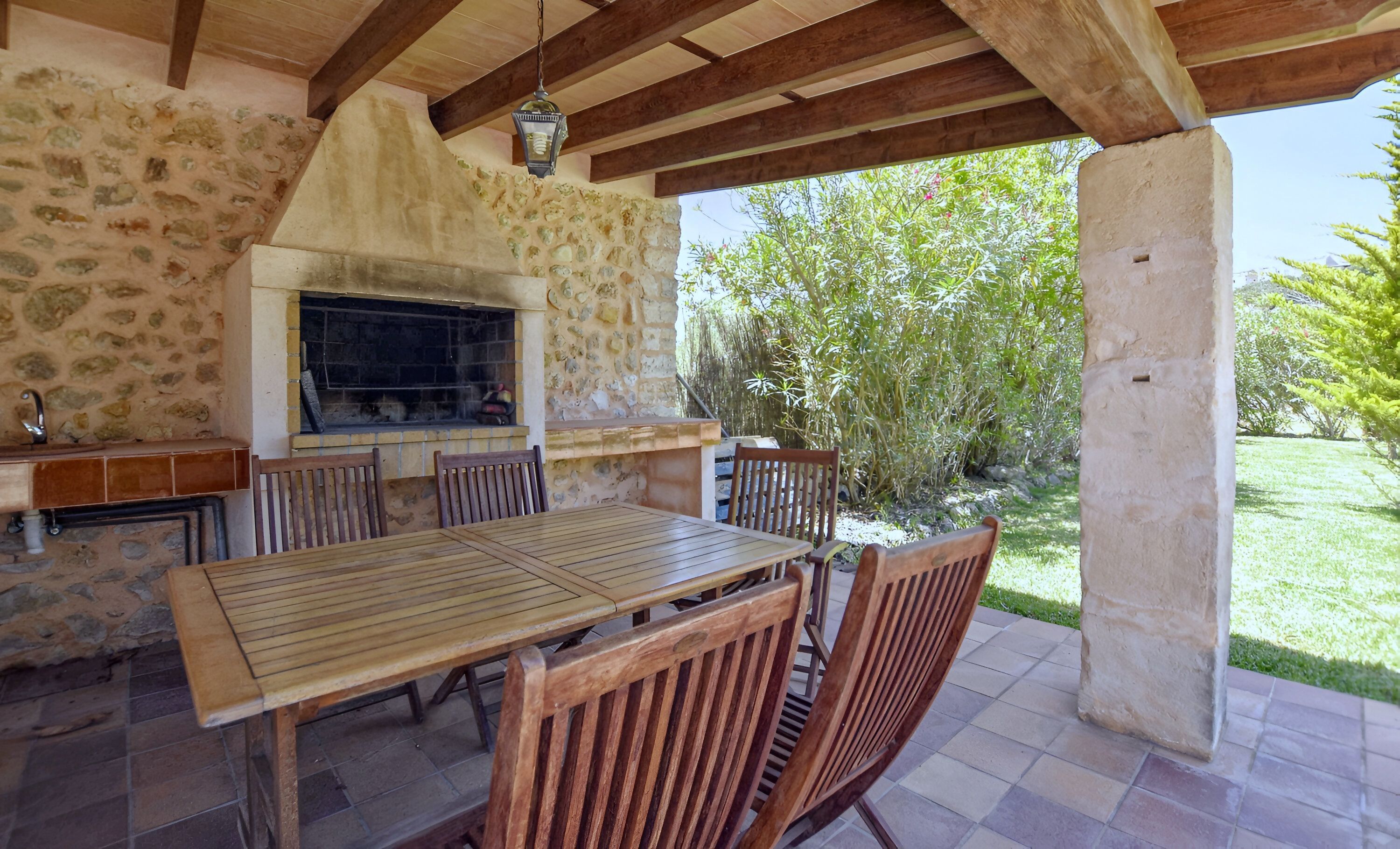 Un patio al aire libre con un muro de piedra, una mesa de madera y sillas.