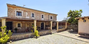 Un edificio de piedra con un patio cubierto, mobiliario exterior y un pequeño jardín.