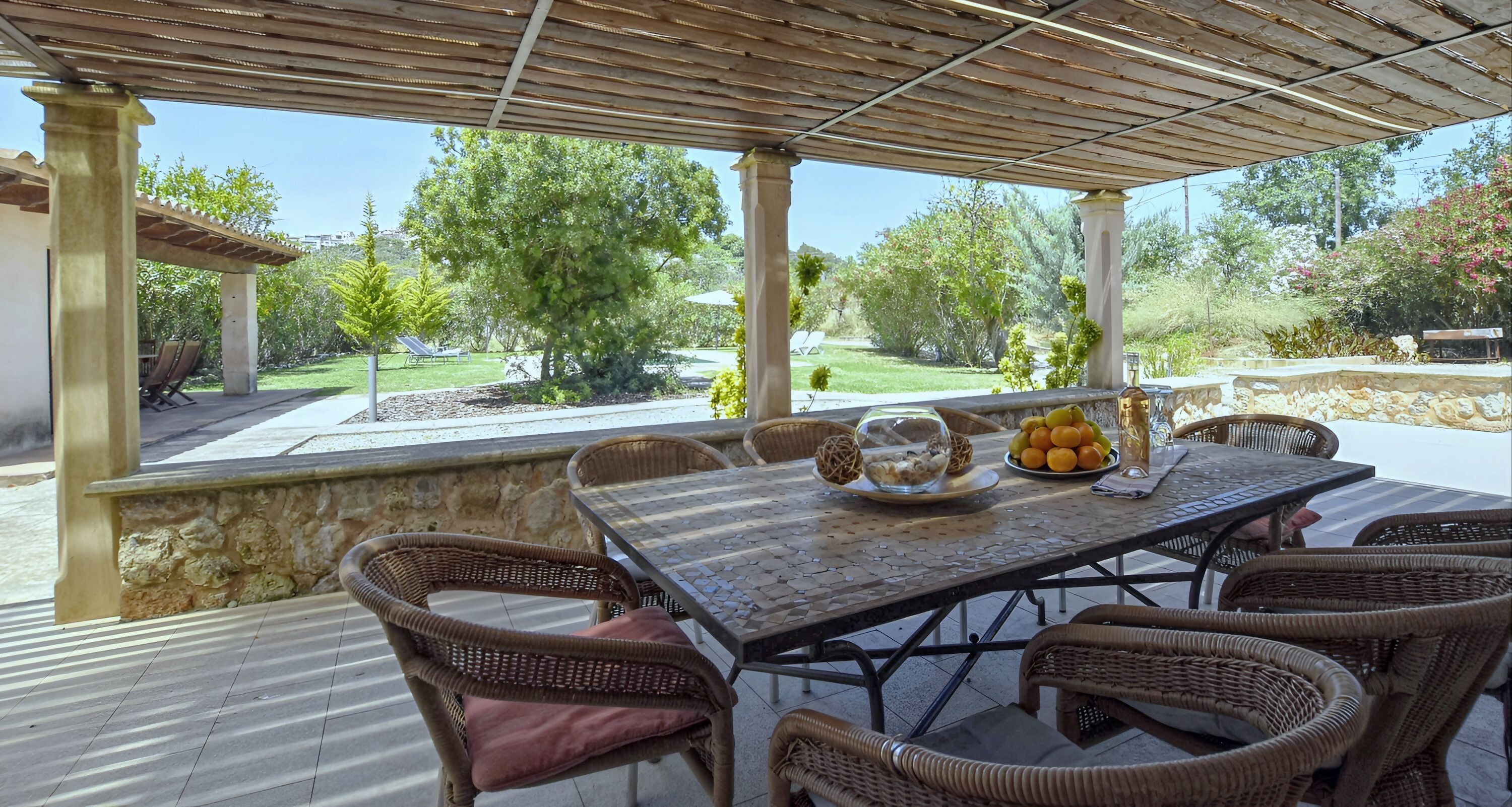 Un patio esterno con tavolo e sedie, una ciotola di frutta e un bicchiere d'acqua.