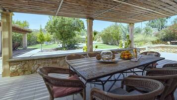 Un patio esterno con tavolo e sedie, una ciotola di frutta e un bicchiere d'acqua.