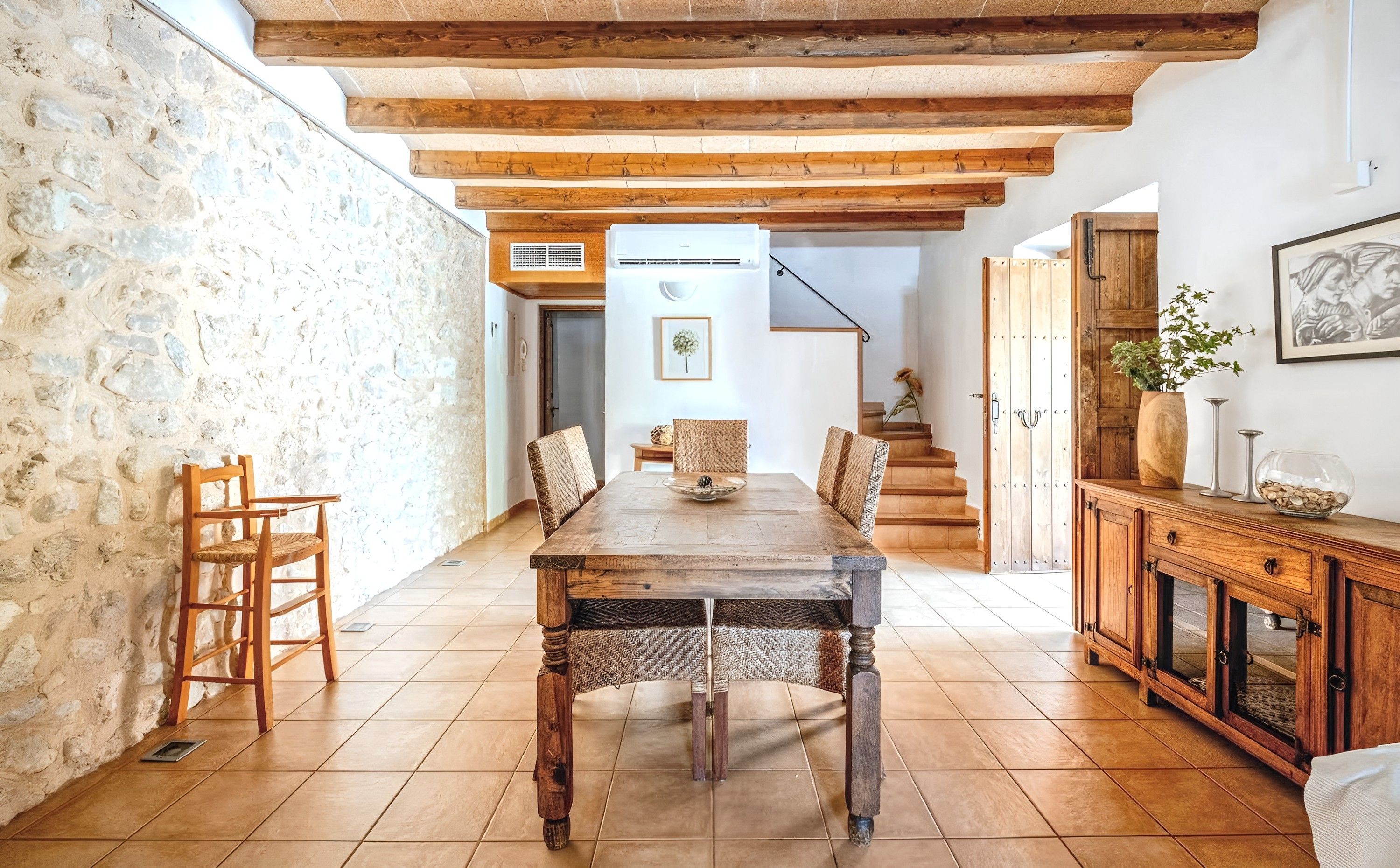 Un comedor rústico con mesa y sillas de madera, paredes de piedra y una escalera que sube a otra habitación.