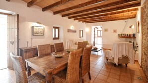 A dining area with a wooden table, wicker chairs, and a stone wall. - Country House 'Cadernera' with Private Pool, Wi-Fi and Air Conditioning (Búger)