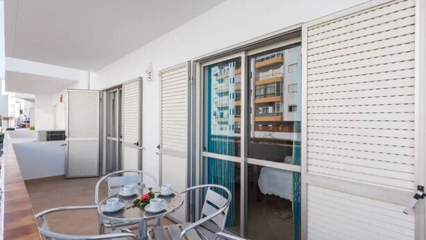 A hotel room with a balcony, a round table with chairs, and a sliding glass door leading to a pool area. - Apartment 'Férias Lagos' with Balcony, Wi-Fi and Air Conditioning (Lagos)