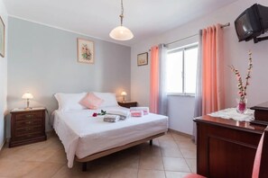 Un dormitorio con cama, mesitas de noche, escritorio, silla, televisor y ventana con cortinas.