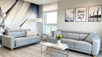 A modern living room with two grey sofas, a white coffee table, and a floor lamp. There are three framed pictures on the wall, one of which says "Have a nice day!"
