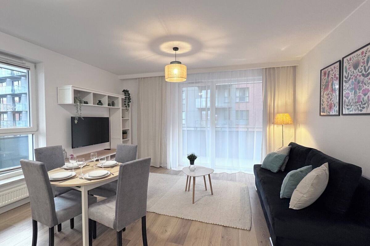 Una sala de estar moderna con comedor, un sofá negro y un televisor montado en la pared.