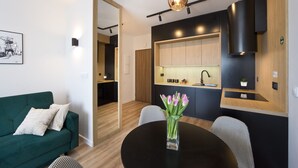A modern kitchen with wooden cabinets, a black countertop, and a black range hood. There is a dining table with a vase of flowers and two chairs. - Bastion Wałowa by Q4Apartments (Gdansk)