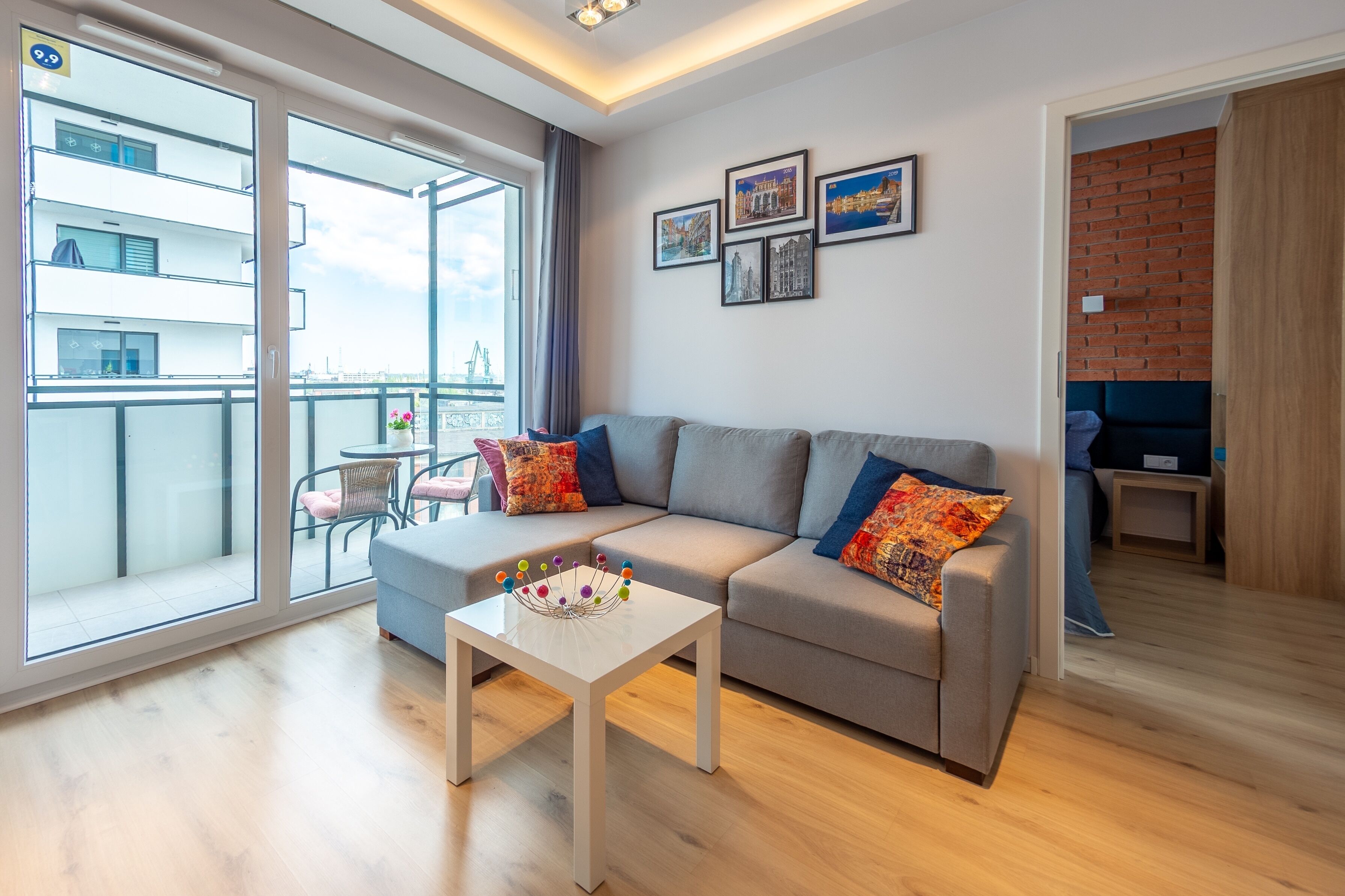 A modern living room with a grey sofa, a white coffee table, and a balcony with a view of a building.