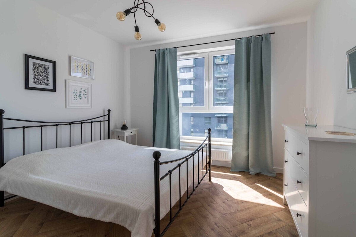 Une chambre à coucher comprenant un lit, une table de chevet, une commode, une fenêtre avec des rideaux et un luminaire au plafond.