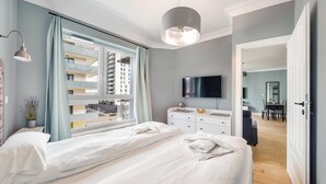 A modern bedroom with a large bed, a TV, and a view of a building outside. - Bastion Wałowa by Q4Apartments (Gdansk)