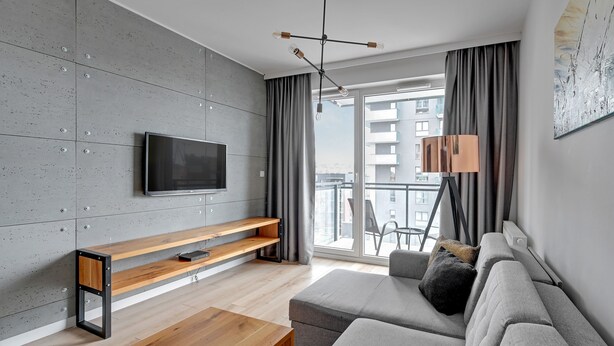 A modern living room with a flat-screen TV, wooden bench, grey sofa, and a floor lamp. - Bastion Wałowa by Q4Apartments (Gdansk)