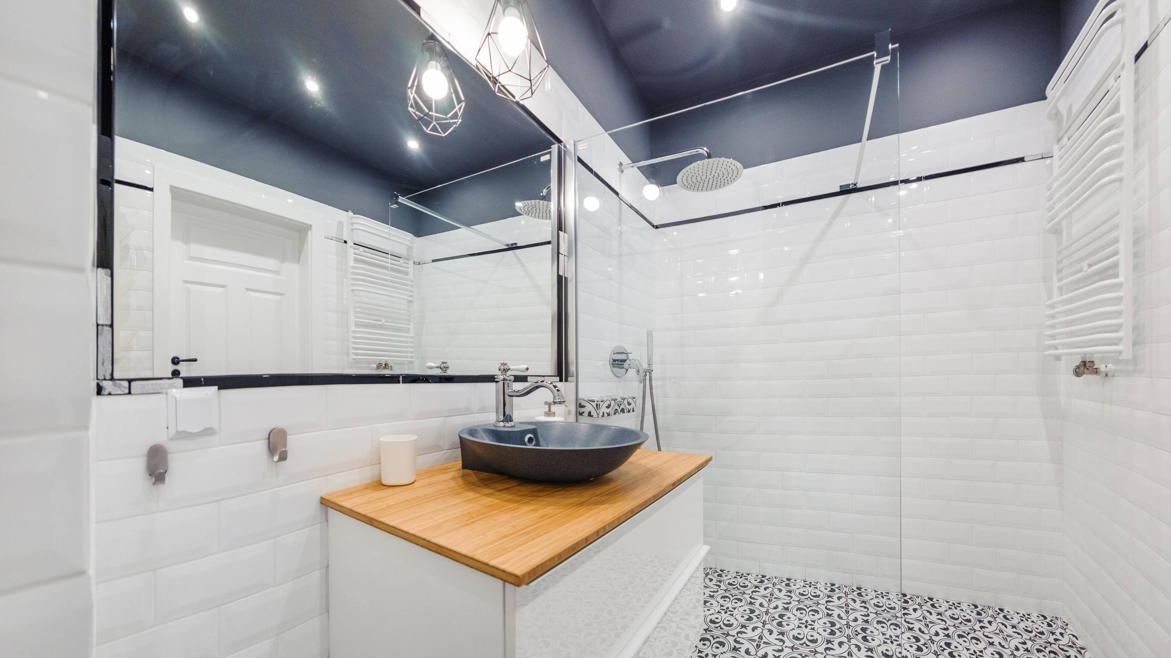 Une salle de bain moderne avec un lavabo sur pied de forme ronde, un grand miroir et une douche à l’italienne.