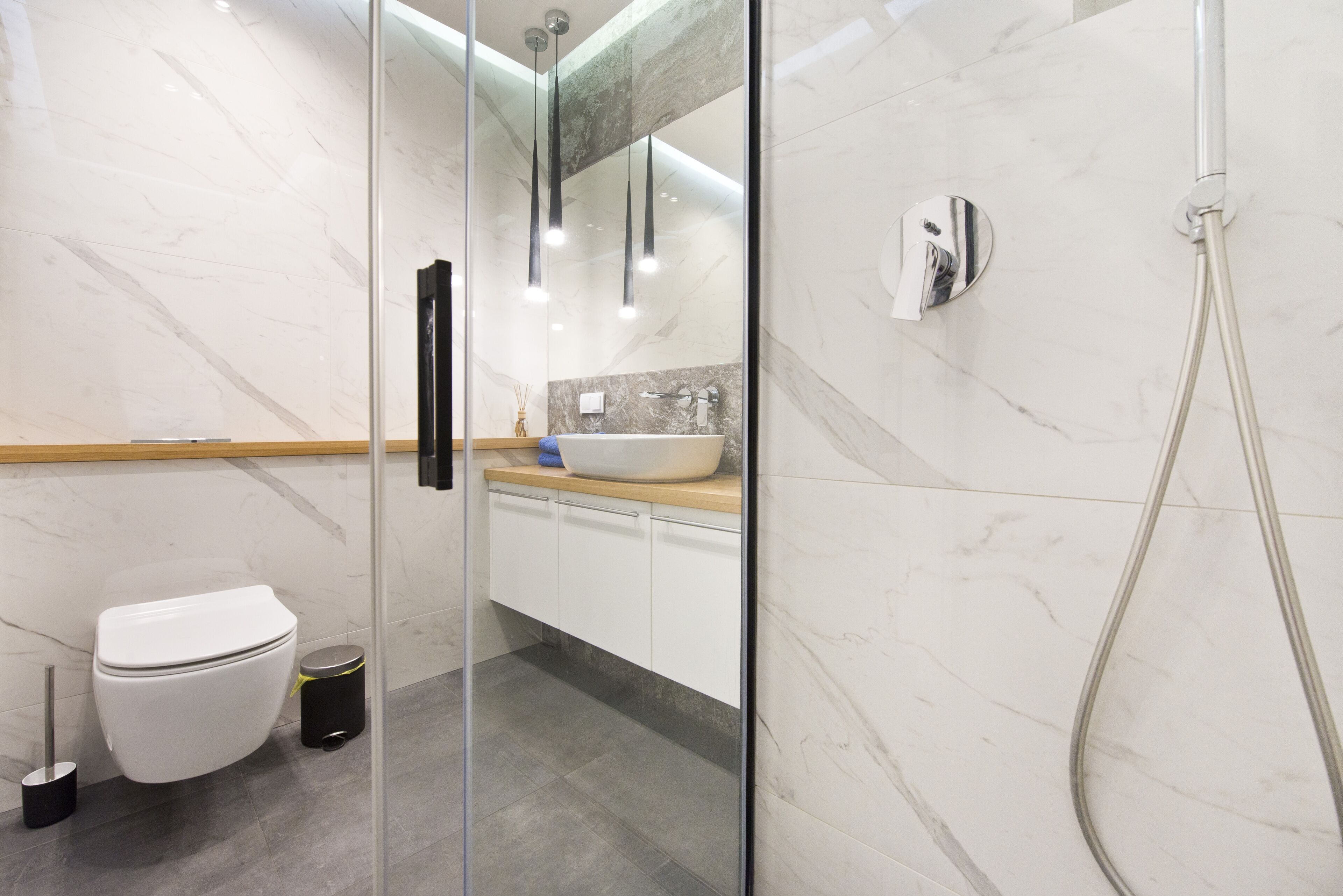 A modern bathroom with a glass shower enclosure, a white toilet, and a marble-tiled floor.