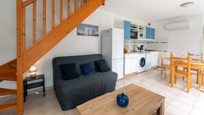Um apartamento moderno com escada de madeira, sofá cinza estampado, mesa de jantar de madeira e cozinha com armários brancos e detalhes azuis.