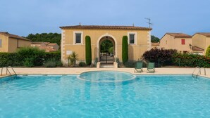 Uma piscina com vista clara da área da piscina, um edifício com entrada em arco e algumas casas próximas.