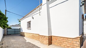 Un edificio blanco con techo de tejas, base de ladrillo y patio empedrado.
