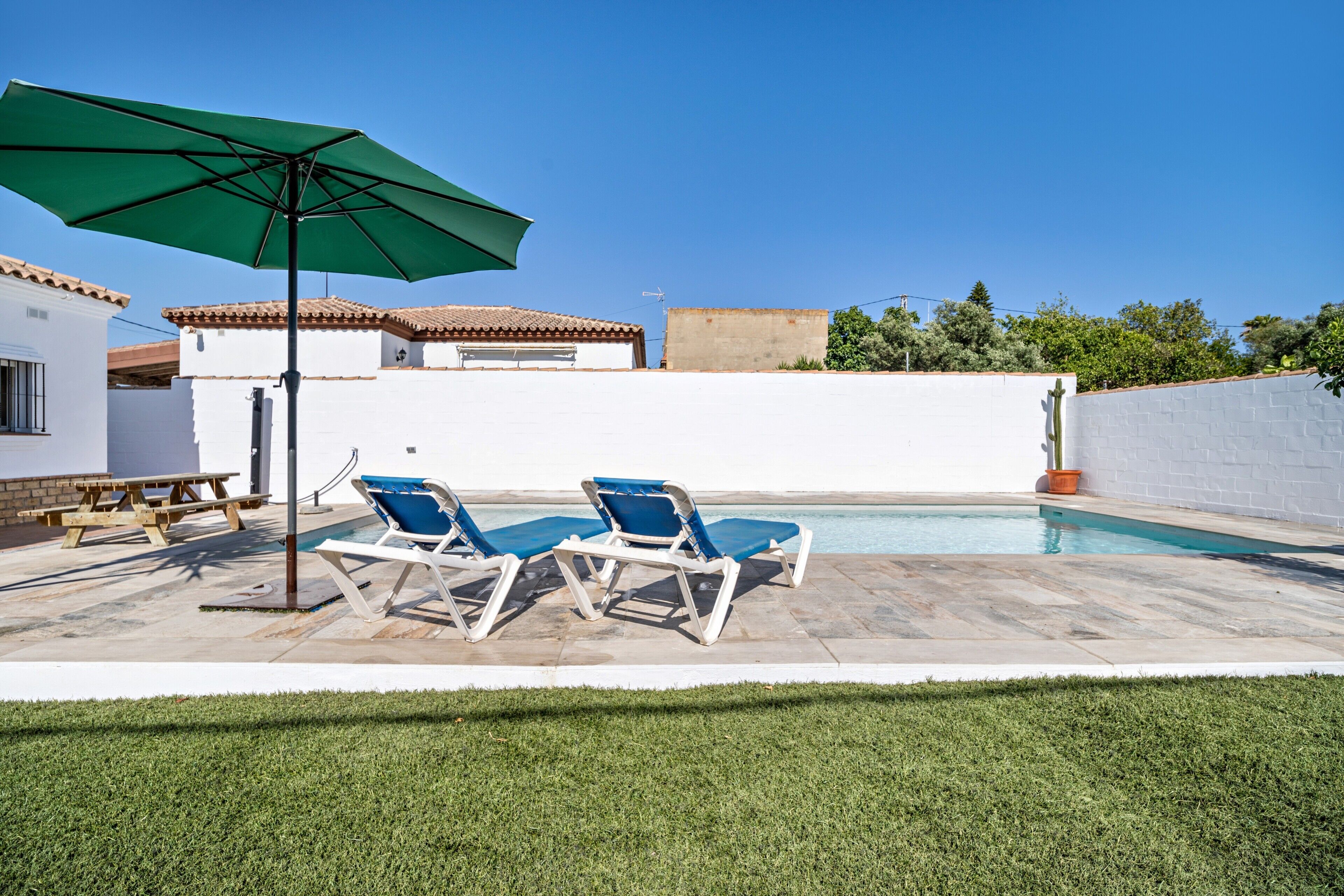 A swimming pool with lounge chairs and a picnic table, surrounded by a white wall and a green lawn.