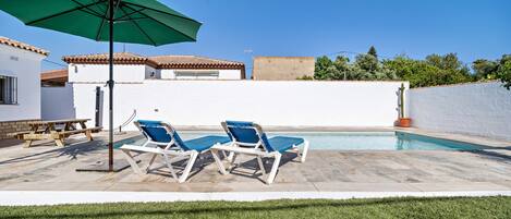 A swimming pool with lounge chairs and a picnic table, surrounded by a white wall and a green lawn.