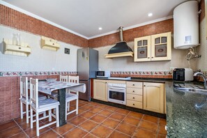 A kitchen with a tiled backsplash, a refrigerator, a microwave, an oven, a sink, and a table with chairs.