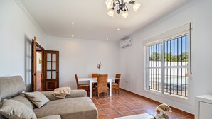 Una sala de estar con un sofá, una mesa de comedor con sillas, una mesita con una figura de Santa, y un ventanal con vistas.