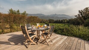 A wooden deck with a round table and chairs, a breakfast setup, and a scenic view of mountains and greenery. - Villa 'Casa Di Pruno' with Private Pool, Wi-Fi and Air Conditioning (Figari)