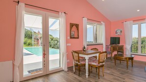 A room with a dining table, chairs, a TV, and a view of a swimming pool. - Holiday Home 'Casetta Maya' with Sea View, Wi-Fi and Air Conditioning (Riparbella)