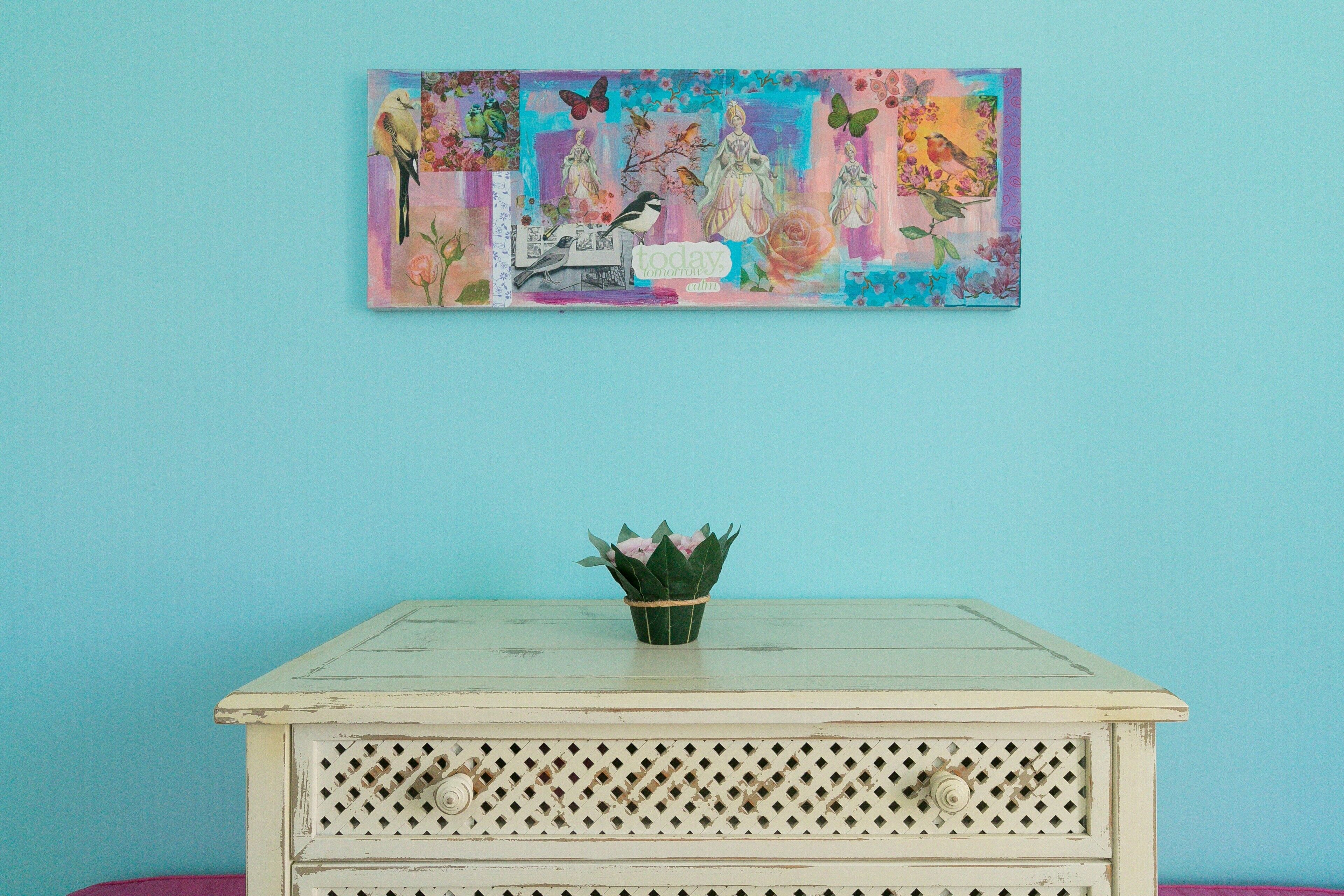 Une pièce avec un mur bleu clair, une table blanche ornée d’une plante verte et une œuvre d’art colorée accrochée au-dessus de la table.