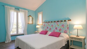 A bedroom with a bed, two nightstands, a window with curtains, a mirror, and a floral-patterned headboard. - Holiday Home 'Casetta Maya' with Sea View, Wi-Fi and Air Conditioning (Riparbella)