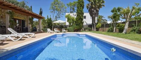 A swimming pool with lounge chairs, a pergola, and a stone wall.