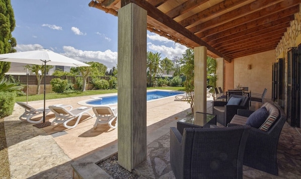 A covered outdoor area with a pool, lounge chairs, and wicker furniture.