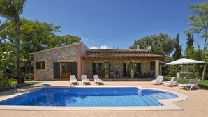 Zona junto a la piscina con un edificio de piedra, sillas de descanso y un cielo azul despejado.