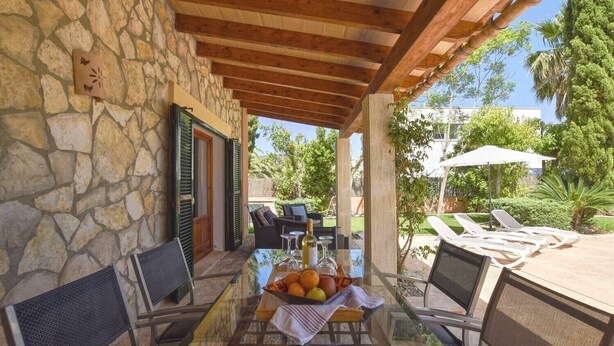 Un patio al aire libre con paredes de piedra, una mesa de vidrio, sillas de mimbre y una sombrilla.