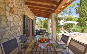 An outdoor patio with stone walls, a glass table, wicker chairs, and a sun umbrella. - Holiday Home 'Correfoc' with Private Pool, Wi-Fi and Air Conditioning (Sa Pobla)