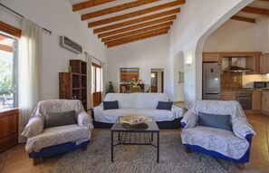 A living room with a sofa, two armchairs, a coffee table, and a kitchen area with a refrigerator and microwave.