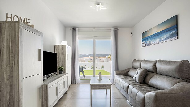 A modern living room with a sofa, TV, and a table. There's a balcony with a view. - Apartment 'Apartamento Poniente' with Sea View, Wi-Fi and Air Conditioning (Zahara de los Atunes)