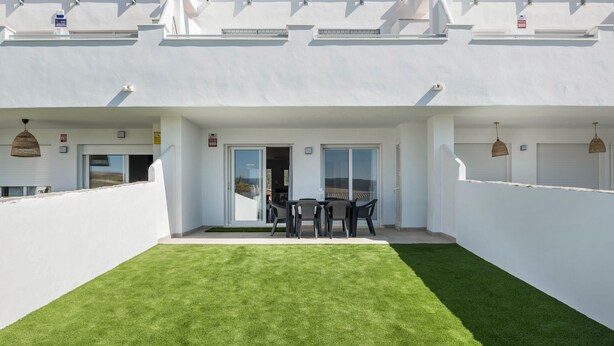 A white building with a flat roof, a covered patio with a table and chairs, and a well-maintained lawn. - Apartment 'Apartamento Poniente' with Sea View, Wi-Fi and Air Conditioning (Zahara de los Atunes)