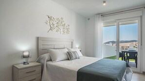A bedroom with a bed, nightstand, lamp, and a view of the outdoors through a sliding door. - Apartment 'Apartamento Poniente' with Sea View, Wi-Fi and Air Conditioning (Zahara de los Atunes)