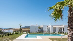 A pool area with a clear view of a white building with multiple balconies, surrounded by greenery and a clear sky. - Apartment 'Apartamento Poniente' with Sea View, Wi-Fi and Air Conditioning (Zahara de los Atunes)