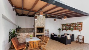 Une terrasse extérieure avec une cheminée en pierre, des meubles en bois et des plantes en pot.
