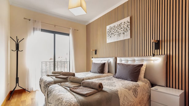 Une chambre avec deux lits, une table de chevet, un porte-manteau et une grande fenêtre avec des rideaux.