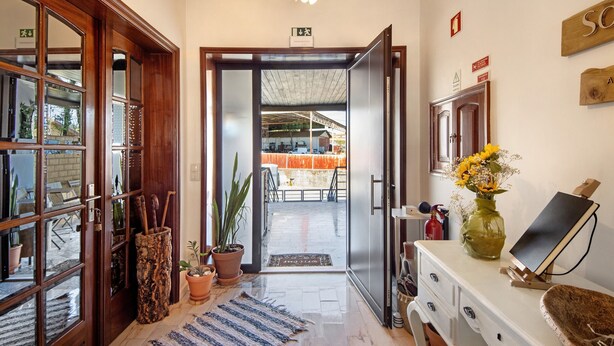 A hotel lobby with a wooden door, a reception desk, a vase with flowers, and a fire extinguisher.