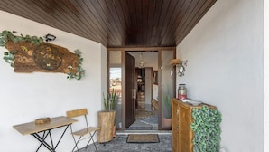 A wooden ceiling, a wall-mounted clock, a wooden table, a bench, a cabinet with greenery, and a statue.