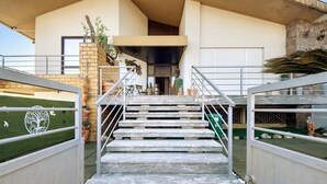 A staircase leading to a building entrance with a stone facade, metal railings, and potted plants.
