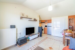Un espace de vie compact comprenant un téléviseur, un meuble de divertissement, une cuisine, un coin repas et une porte donnant sur une autre pièce.