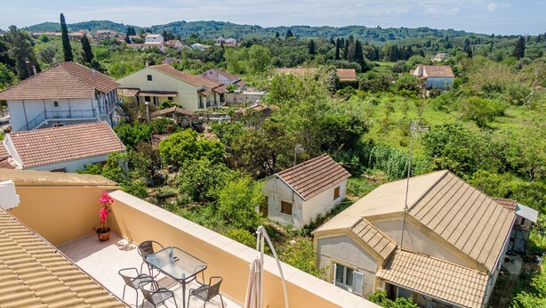 Un quartier résidentiel avec des maisons, une terrasse dotée d’une table et de chaises, et une vue sur la verdure environnante.