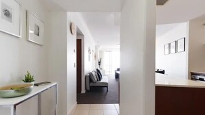 A hallway with a modern kitchen area, a dining table with a bowl and plant, and a sofa in the background.