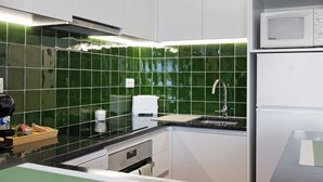Une cuisine avec des carreaux verts, un four à micro-ondes, un évier et une machine à café.