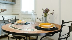 A round dining table with a mosaic tile design, surrounded by black chairs. A metal pitcher with flowers and a water bottle are on the table. - Holiday Home 'Pullin' with Private Garden and Wi-Fi (Carasco)