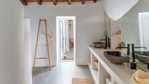 Une salle de bain avec une échelle en bois, un grand miroir, un lavabo en pierre et une vue sur une autre pièce.